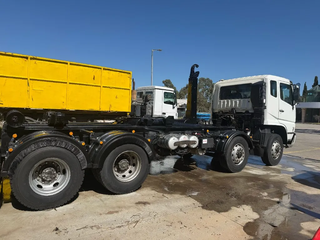 Clean white hook-lift truck parked on wet concrete after washing