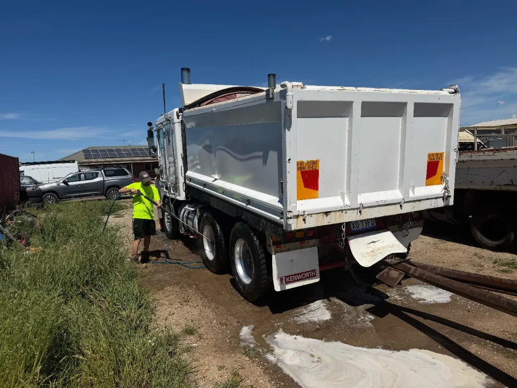 Operator pressure-washing a white Kenworth tipper truck on site